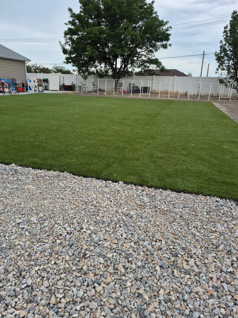 Residential backyard with a full artificial turf lawn edged crisply against a gravel border