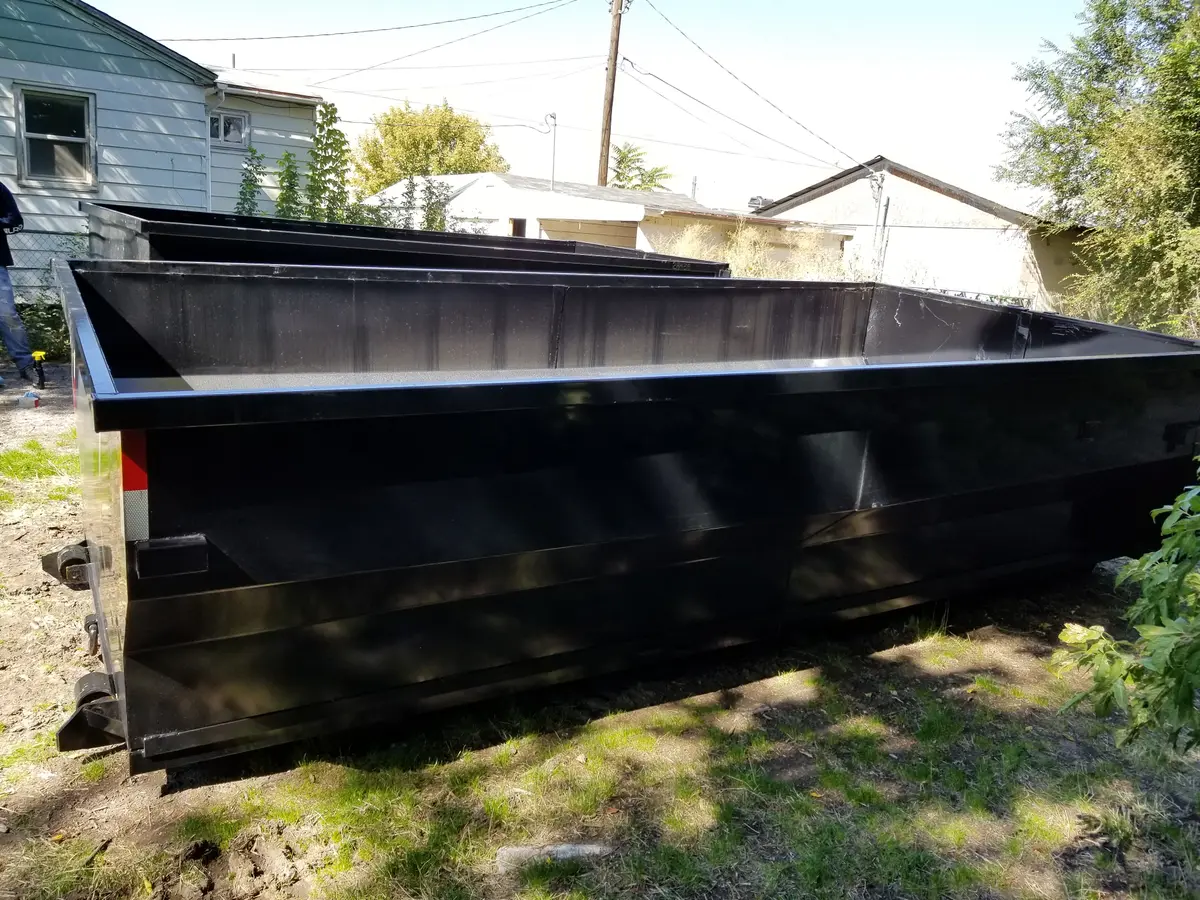 Side view of an empty black roll-off dumpster showing its full length, open top, and interior depth