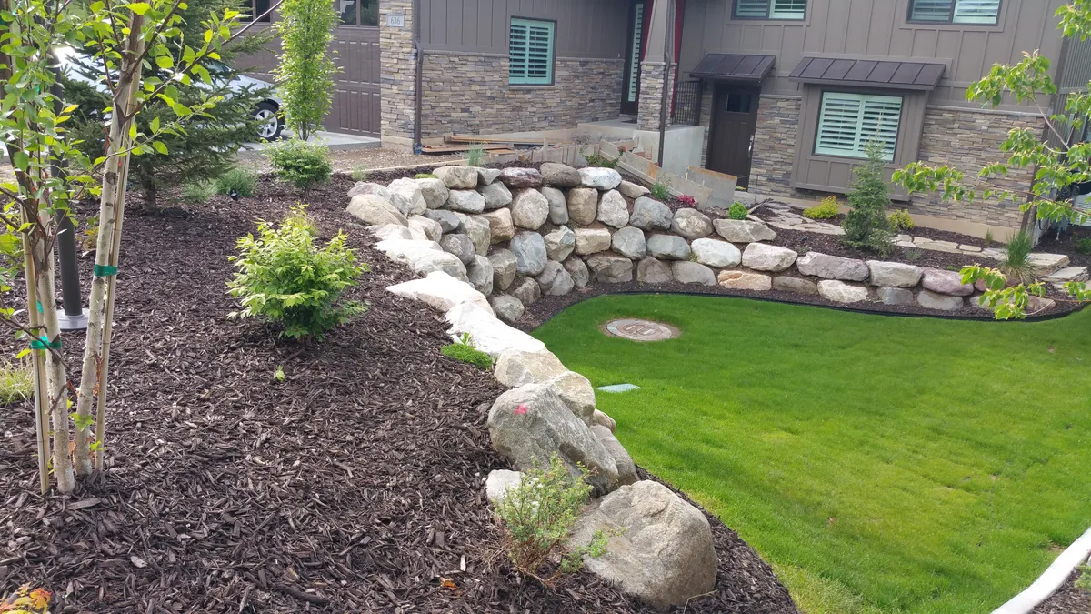 Finished Salt Lake County yard — fresh sod, a boulder retaining wall, mulched beds, and newly planted trees