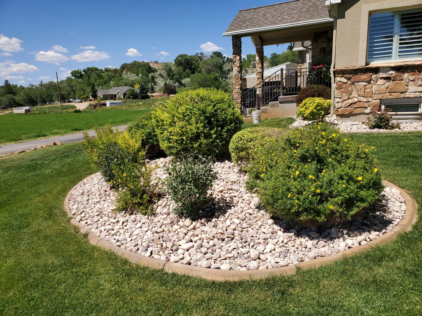 Finished SLC landscaping — a curbed rock bed with shaped shrubs in front of the home