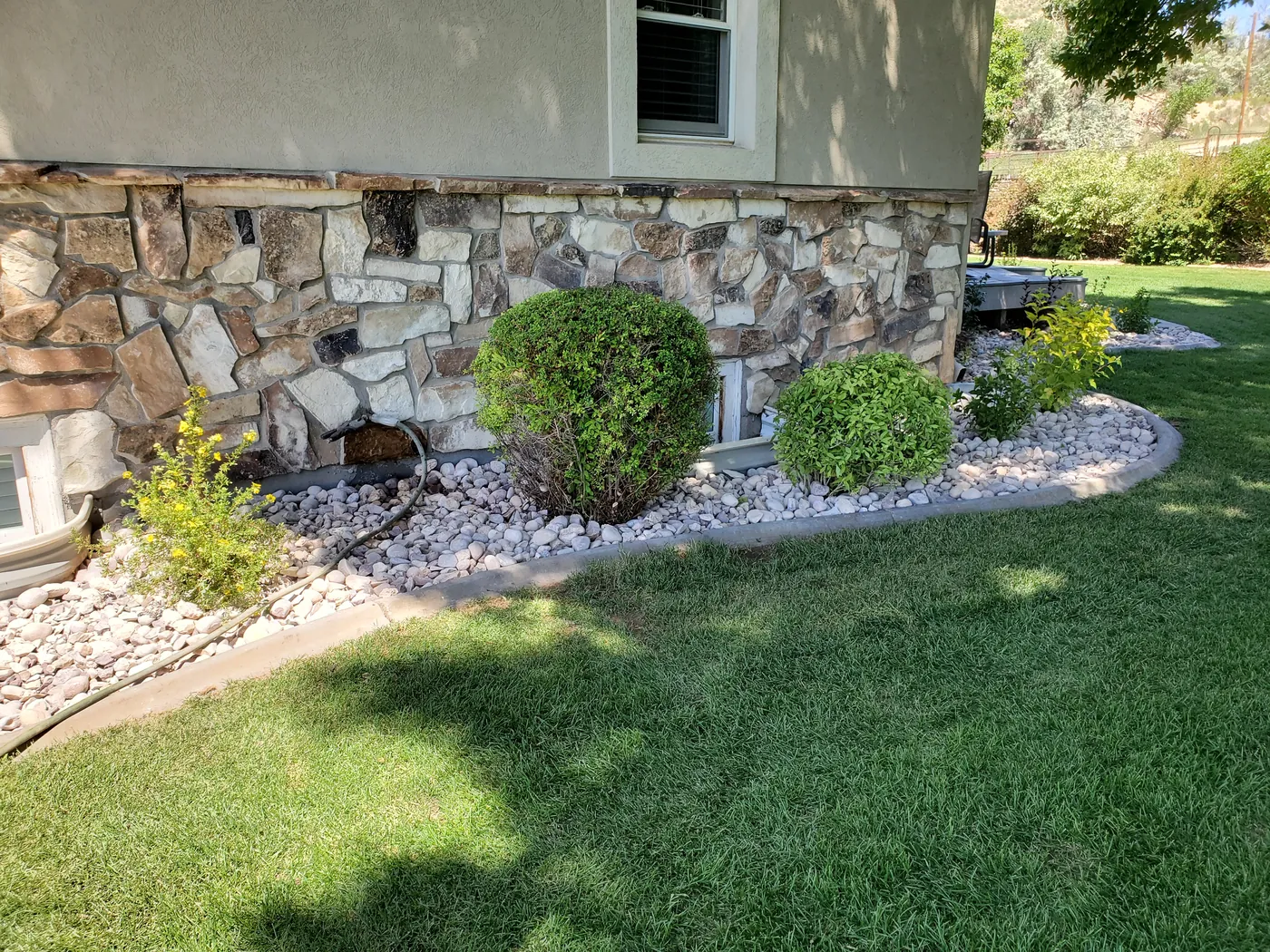 Tidy rock border and shaped shrubs running along the foundation with a fresh-cut lawn