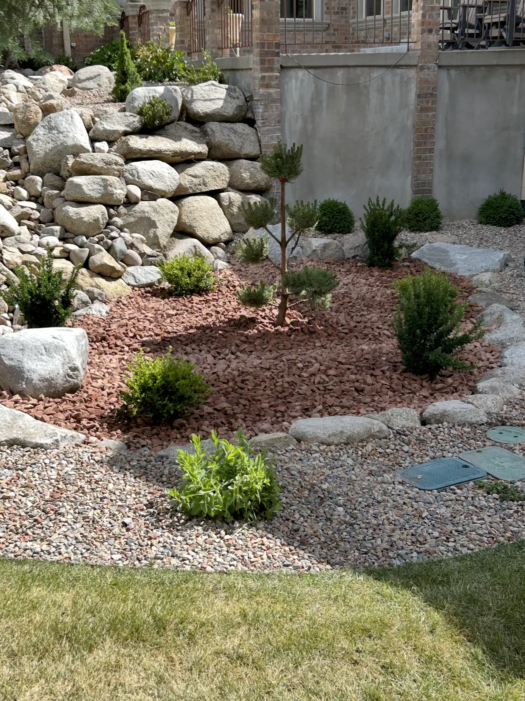 Close view of a red-stone planting bed edged with large boulders beside a river-rock dry creek bed