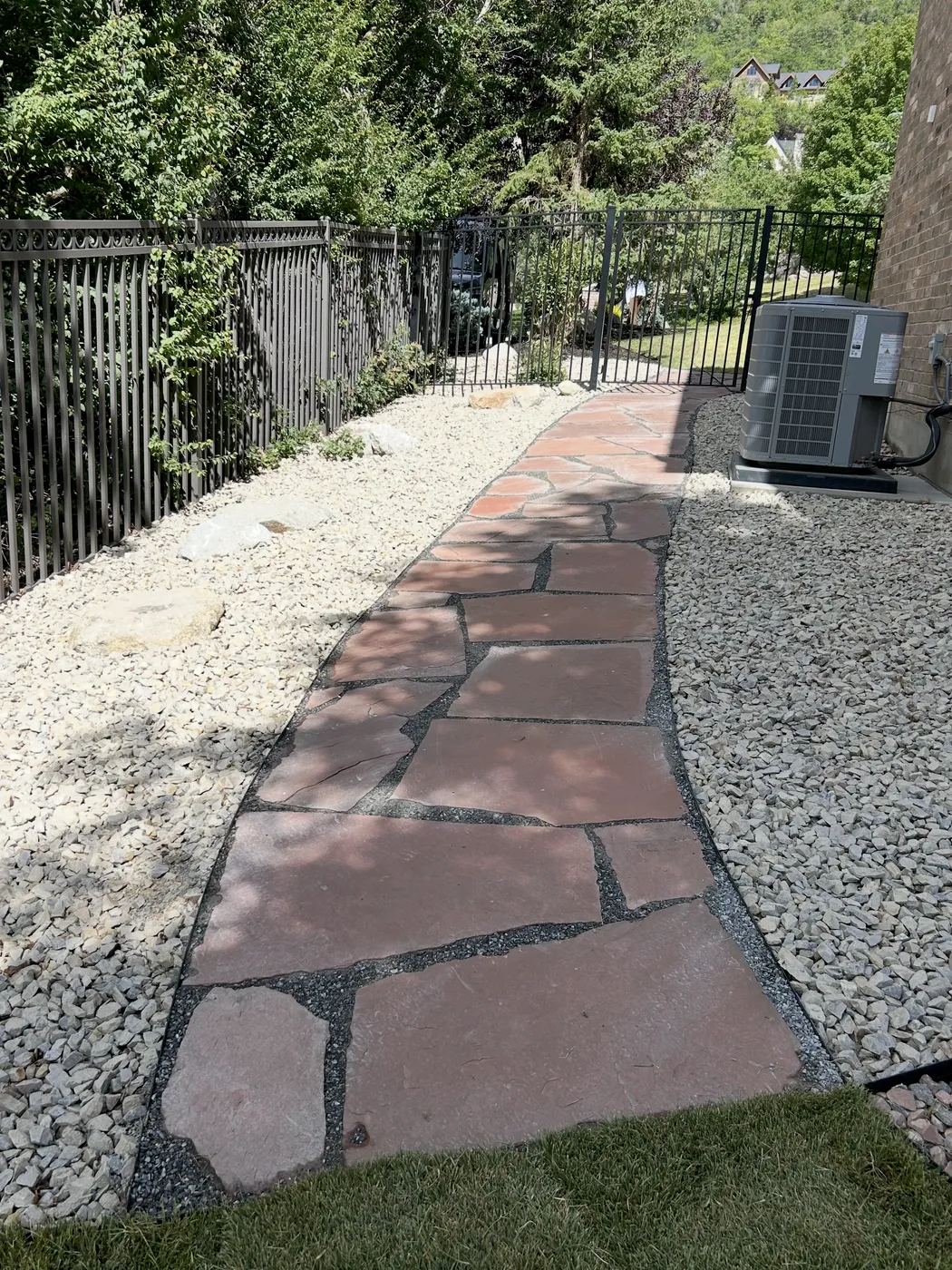 Natural flagstone walkway running between a river-rock bed and a wrought-iron fence