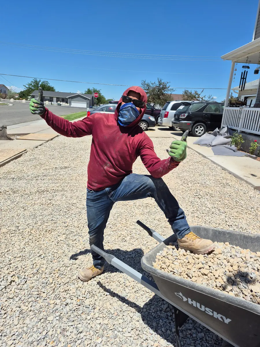 A crew member giving two thumbs up beside a wheelbarrow of drainage rock on the finished front yard