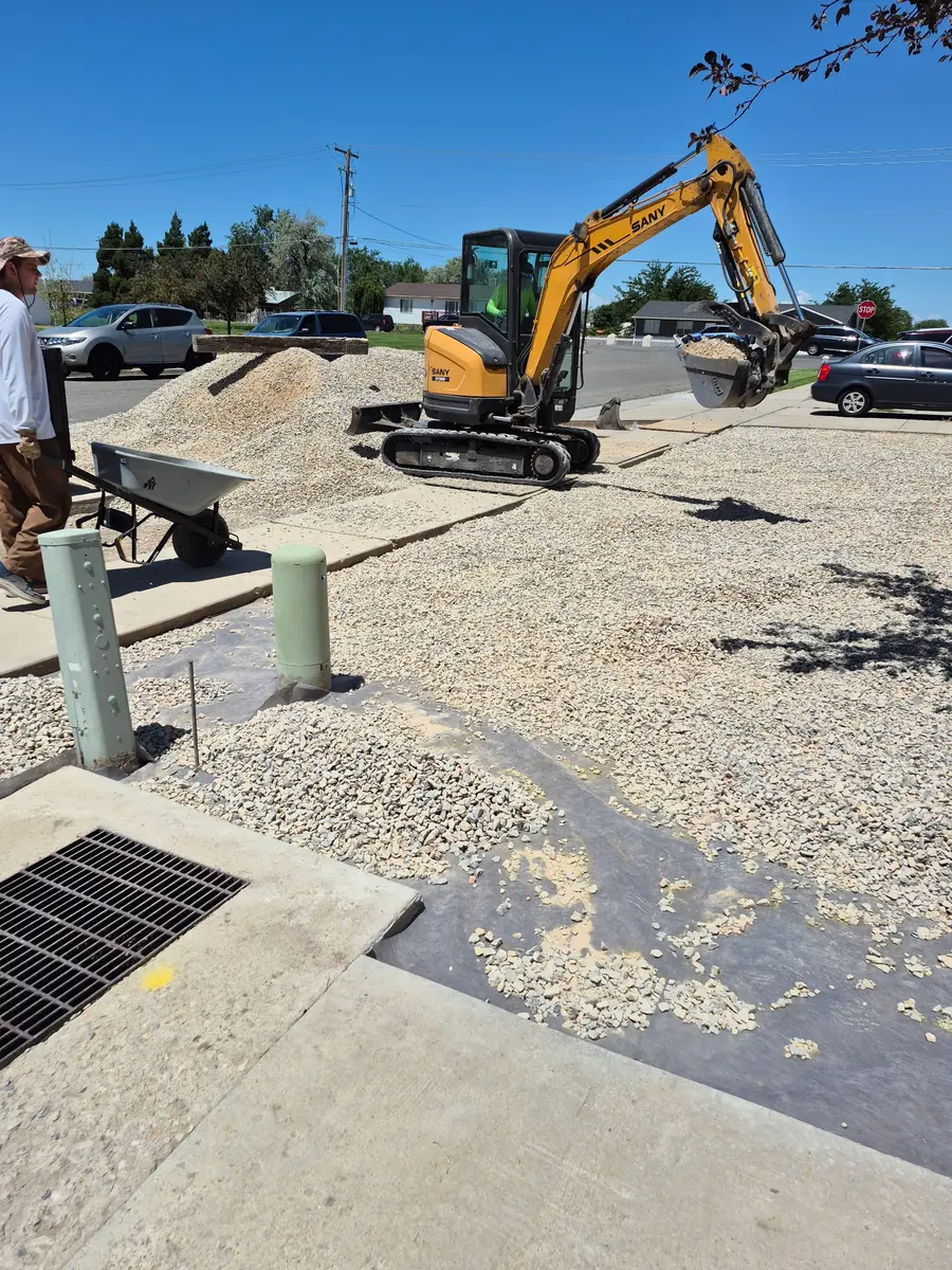 A mini-excavator spreading drainage rock across the front yard with construction mats laid over the walkway