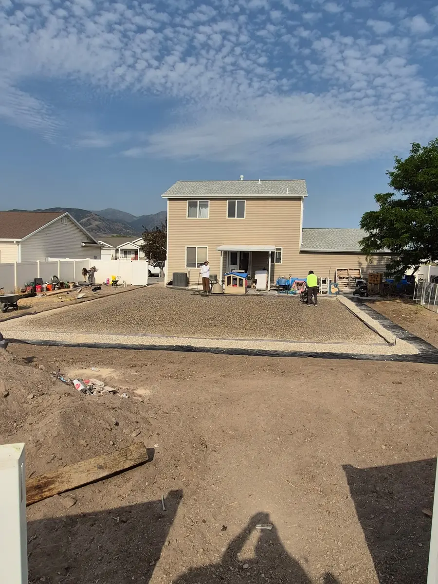 The backyard regraded to a squared-off, compacted rock base ready for turf, with mountains behind the house