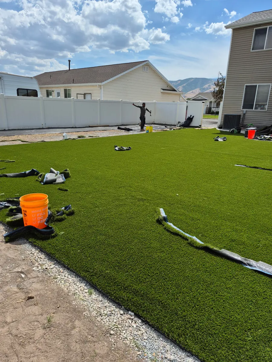 Artificial turf laid across the full width of the backyard against a white vinyl fence with mountains beyond